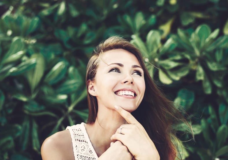 Attractive woman smiling in front of a leafy green background