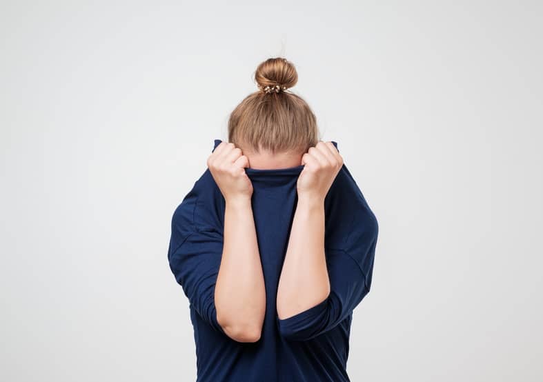 A young woman hiding her face in her sweater because she's embarrassed about acne