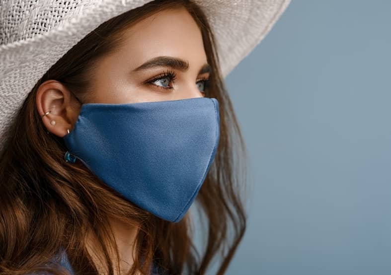 A young woman wears a blue face mask and white hat 