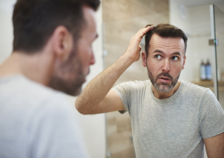 image of man looking into a mirror at his thinning hair