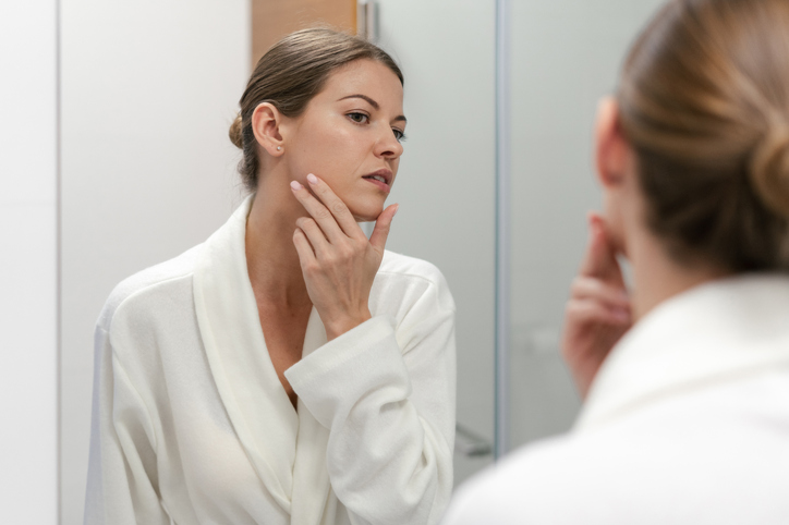 Woman in a bath robe checking her skin in the mirror.